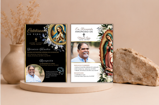 Two printed memorial or celebration cards displayed side by side on a round wooden stand, styled with dried flowers in a vase and a rock against a warm beige background. The left card is predominantly black with gold and white text and religious artwork; the right card is white with a portrait photo, gold text, and a colorful Virgin of Guadalupe illustration.